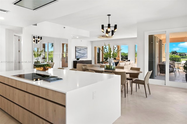 kitchen featuring hanging light fixtures, a wealth of natural light, a kitchen island, black electric cooktop, and a chandelier