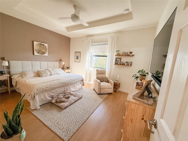 bedroom with a raised ceiling, ceiling fan, and light wood-type flooring