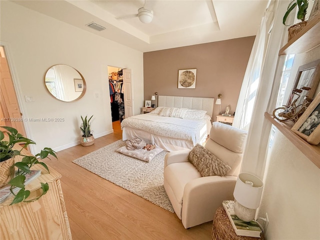 bedroom featuring a tray ceiling, a walk in closet, ceiling fan, light hardwood / wood-style floors, and a closet