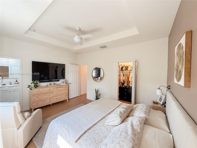 bedroom with a closet, a walk in closet, light hardwood / wood-style floors, and a tray ceiling