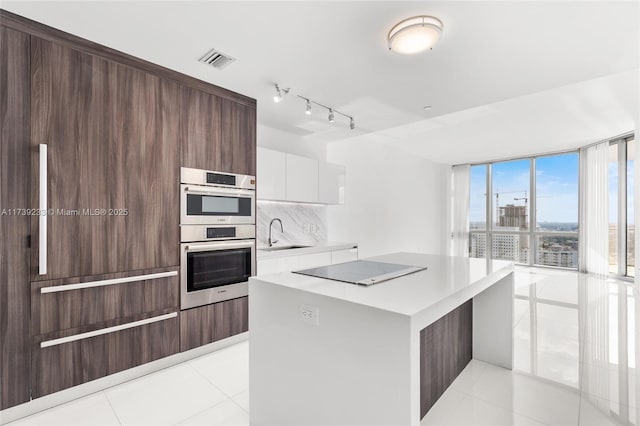 kitchen with tasteful backsplash, light tile patterned floors, black electric cooktop, double oven, and white cabinets