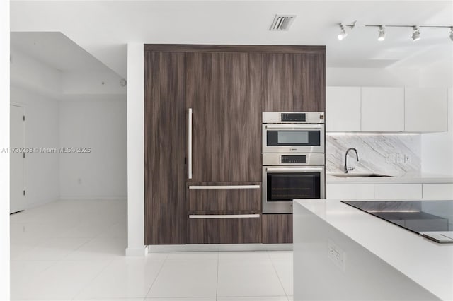 kitchen with double oven, tasteful backsplash, sink, white cabinets, and black electric stovetop