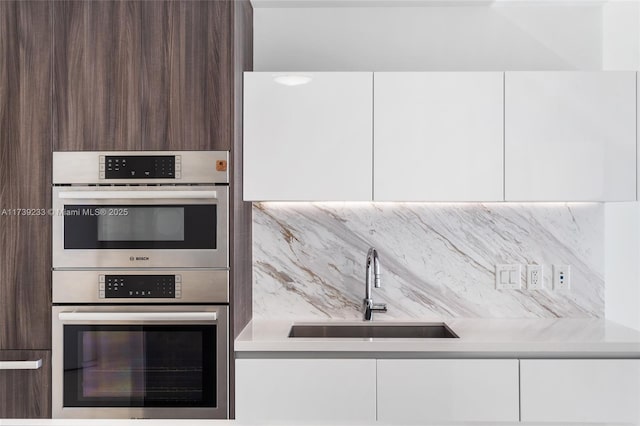 kitchen featuring stainless steel double oven, dark brown cabinetry, sink, and white cabinets