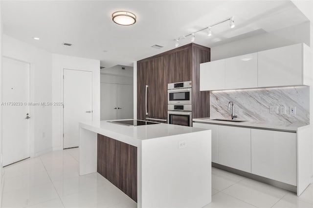 kitchen with double oven, sink, white cabinets, and a kitchen island