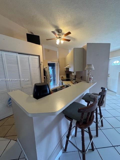 kitchen featuring a kitchen breakfast bar, light tile patterned floors, ceiling fan, kitchen peninsula, and a textured ceiling