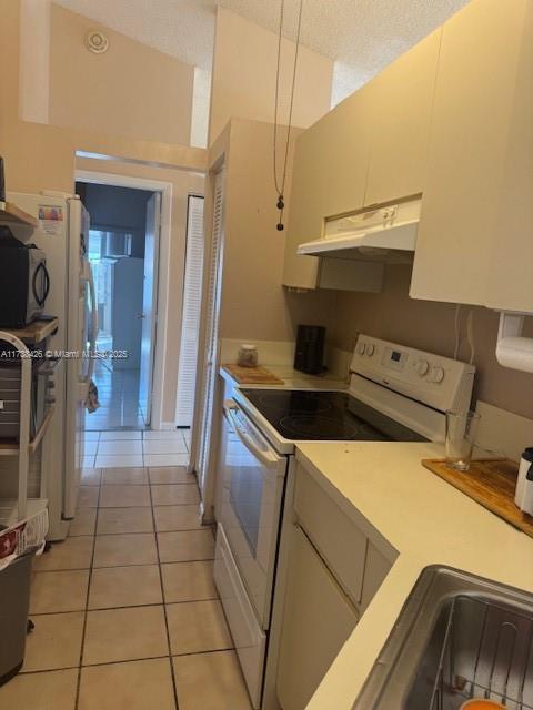 kitchen featuring white appliances, white cabinetry, a textured ceiling, light tile patterned flooring, and vaulted ceiling