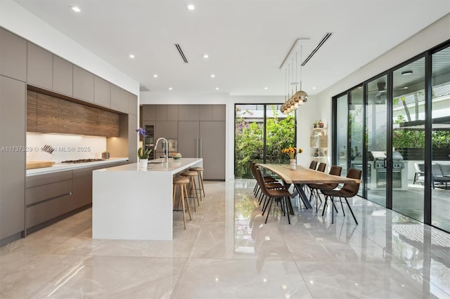 kitchen featuring a breakfast bar, sink, gas stovetop, hanging light fixtures, and a kitchen island with sink