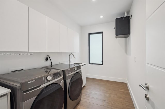 clothes washing area featuring cabinets, sink, washing machine and dryer, and light wood-type flooring