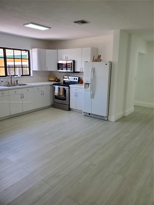 kitchen with sink, white cabinets, backsplash, stainless steel appliances, and light hardwood / wood-style flooring