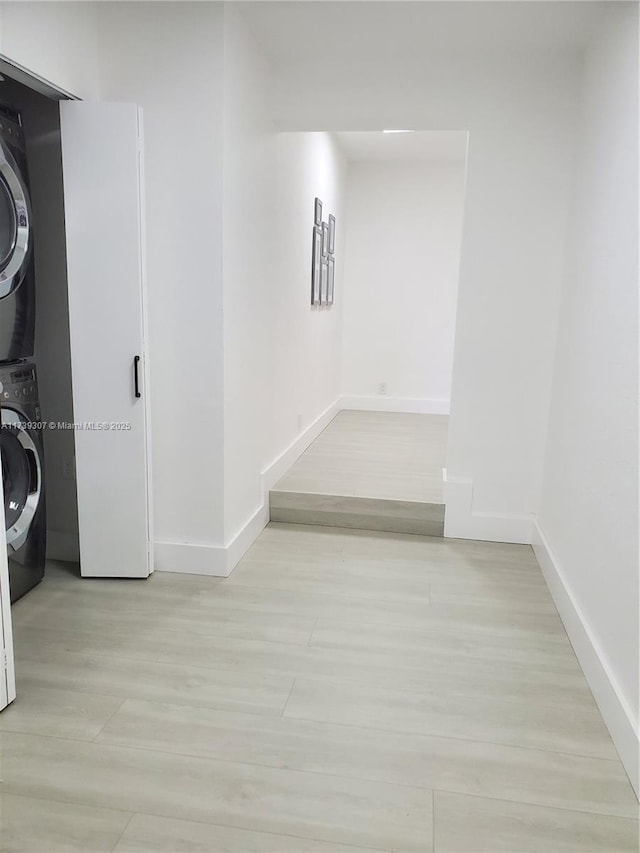 hallway with stacked washer / drying machine and light wood-type flooring