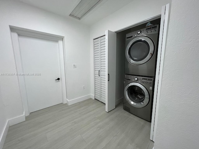 laundry area with stacked washer / drying machine and light hardwood / wood-style flooring