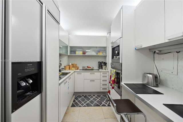 kitchen with light tile patterned floors, built in refrigerator, white cabinets, decorative backsplash, and oven