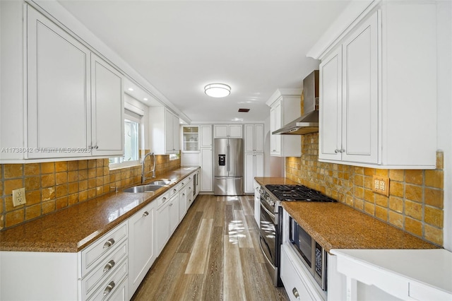 kitchen featuring wall chimney range hood, appliances with stainless steel finishes, white cabinets, and a sink