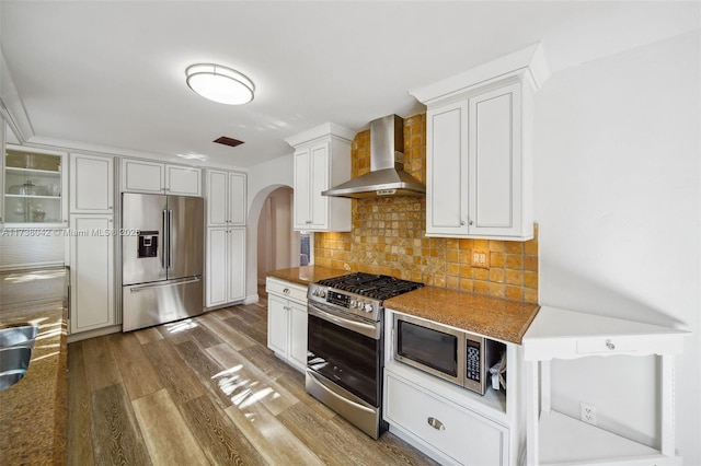 kitchen with tasteful backsplash, appliances with stainless steel finishes, white cabinets, wood finished floors, and wall chimney exhaust hood