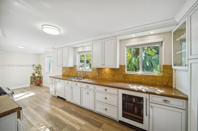 kitchen with glass insert cabinets, light wood-style floors, white cabinets, a sink, and beverage cooler