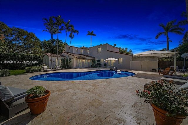 pool at dusk with an outdoor structure, a patio area, fence, and a storage shed