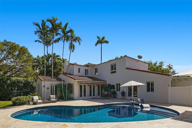 rear view of house featuring an outdoor pool, a patio, fence, french doors, and stucco siding