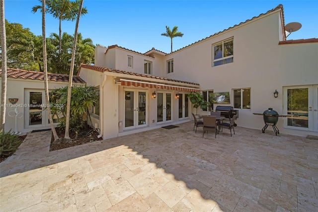 rear view of property with a tile roof, french doors, a patio area, and stucco siding