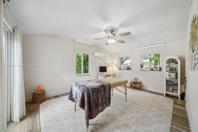 bedroom with vaulted ceiling, an AC wall unit, light wood-type flooring, and baseboards