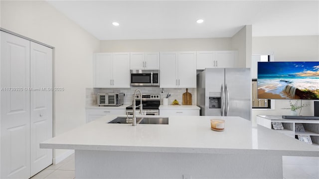 kitchen featuring sink, an island with sink, stainless steel appliances, decorative backsplash, and white cabinets