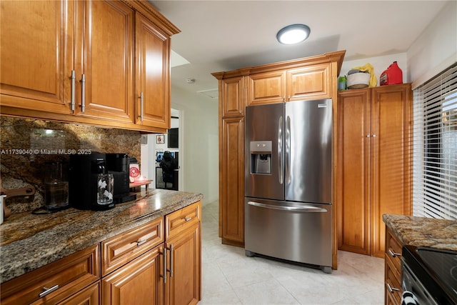 kitchen featuring light tile patterned floors, decorative backsplash, stainless steel fridge, and dark stone counters