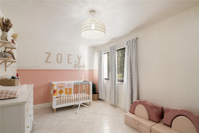 bedroom featuring light tile patterned flooring, a nursery area, and a textured ceiling