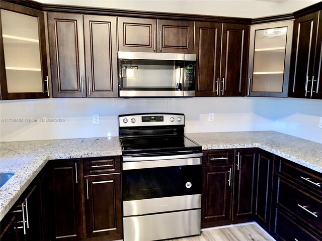 kitchen with appliances with stainless steel finishes, light stone counters, dark brown cabinetry, and light hardwood / wood-style flooring