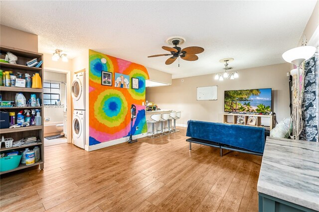 interior space featuring stacked washer and dryer, ceiling fan with notable chandelier, hardwood / wood-style floors, and a textured ceiling