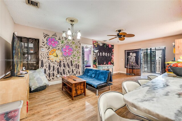 living room featuring ceiling fan with notable chandelier, a textured ceiling, and light wood-type flooring