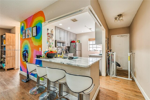 kitchen featuring sink, light wood-type flooring, appliances with stainless steel finishes, kitchen peninsula, and light stone countertops