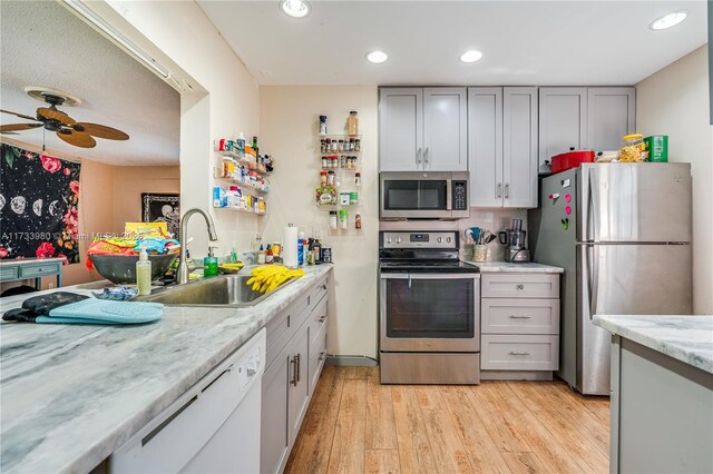 kitchen featuring sink, light hardwood / wood-style flooring, ceiling fan, stainless steel appliances, and light stone countertops