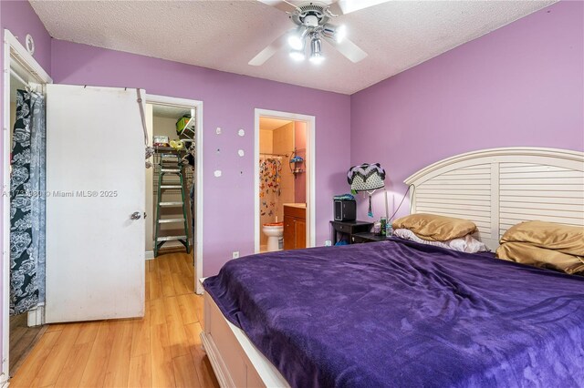 bedroom with connected bathroom, a spacious closet, light hardwood / wood-style flooring, and a textured ceiling