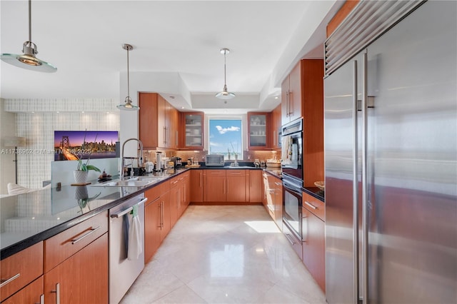 kitchen featuring a sink, backsplash, stainless steel appliances, glass insert cabinets, and hanging light fixtures