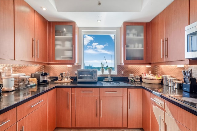 kitchen featuring stainless steel microwave, backsplash, and dark stone counters