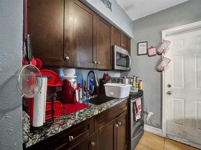 kitchen featuring sink, light tile patterned floors, appliances with stainless steel finishes, dark stone countertops, and dark brown cabinetry