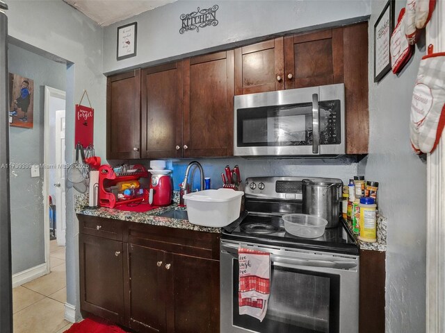 kitchen with light tile patterned flooring, appliances with stainless steel finishes, dark brown cabinets, and light stone counters