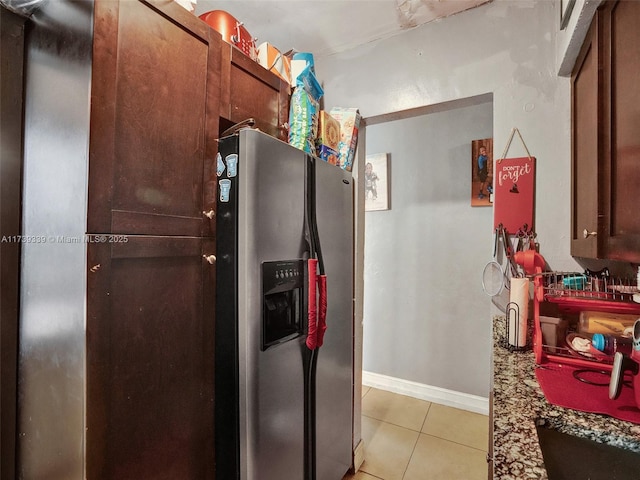 kitchen featuring stainless steel refrigerator with ice dispenser, light tile patterned flooring, and dark stone countertops