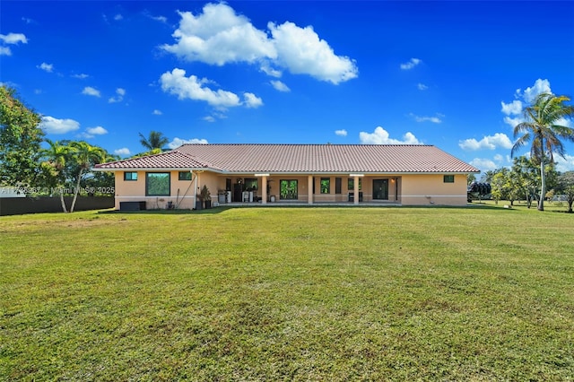 rear view of house featuring a tiled roof, a lawn, and stucco siding