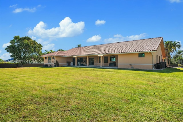 rear view of property featuring a tiled roof, a lawn, central AC unit, and stucco siding