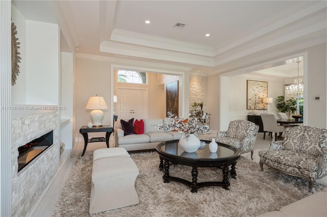 living room featuring a raised ceiling, ornamental molding, a chandelier, and a tile fireplace