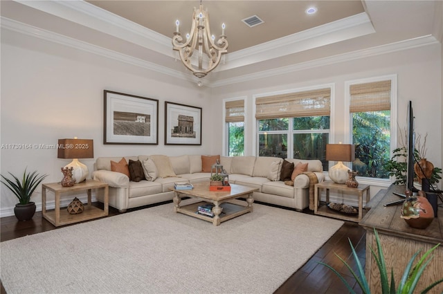 living room featuring a raised ceiling, ornamental molding, hardwood / wood-style floors, and a notable chandelier