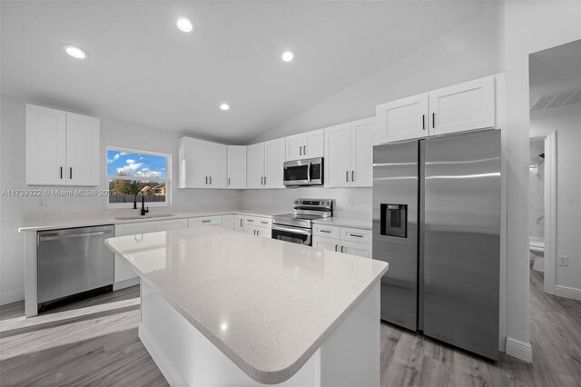 kitchen featuring a kitchen island, white cabinetry, lofted ceiling, sink, and stainless steel appliances