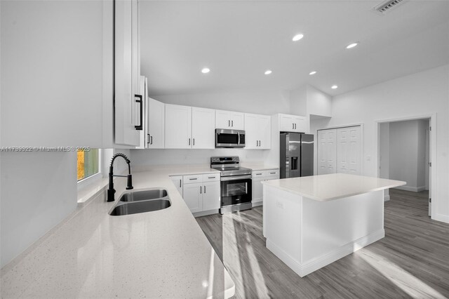 kitchen featuring vaulted ceiling, a kitchen island, appliances with stainless steel finishes, sink, and white cabinets