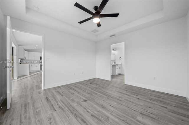 empty room featuring ceiling fan, a tray ceiling, and light wood-type flooring