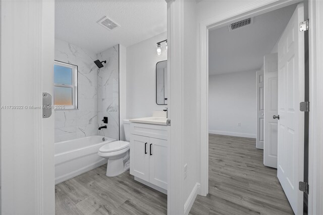 full bathroom with vanity, wood-type flooring, a textured ceiling, tiled shower / bath, and toilet