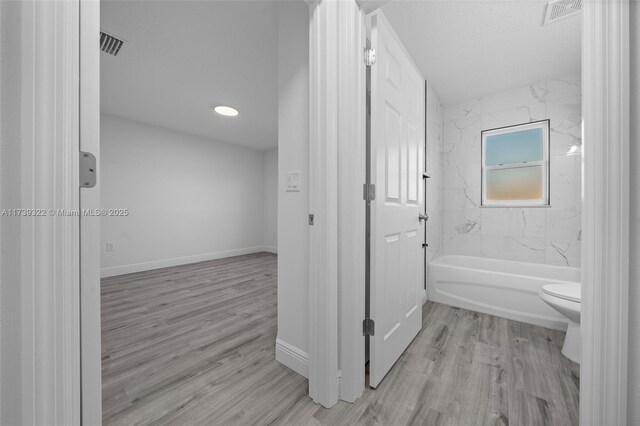 bathroom with tiled shower / bath, hardwood / wood-style flooring, and toilet