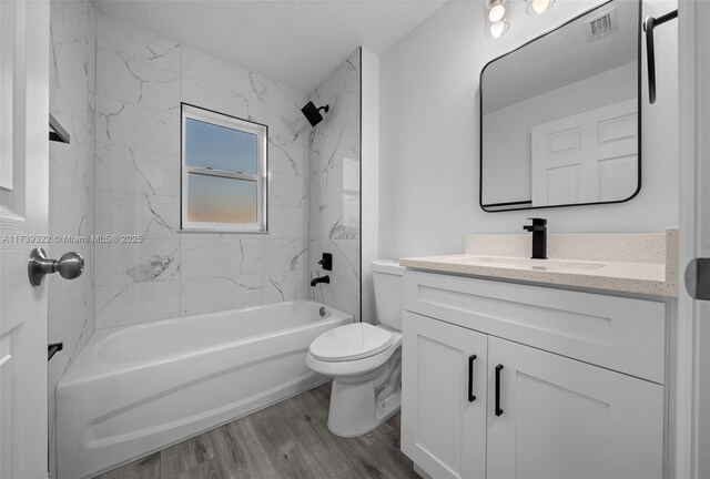 full bathroom featuring hardwood / wood-style floors, vanity, a textured ceiling, tiled shower / bath, and toilet