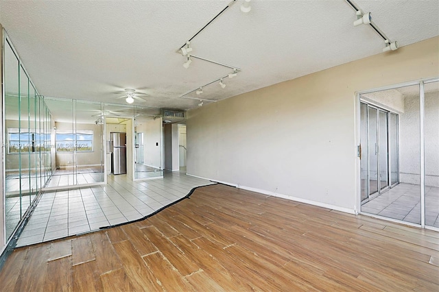 spare room with rail lighting, wood finished floors, a ceiling fan, a textured ceiling, and baseboards