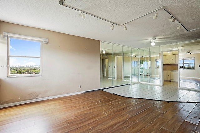 unfurnished room featuring rail lighting, wood finished floors, ceiling fan, plenty of natural light, and a textured ceiling