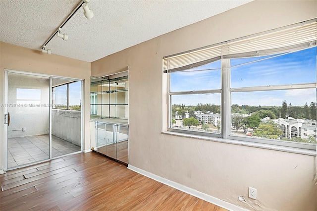 unfurnished bedroom with track lighting, wood finished floors, a textured ceiling, and baseboards